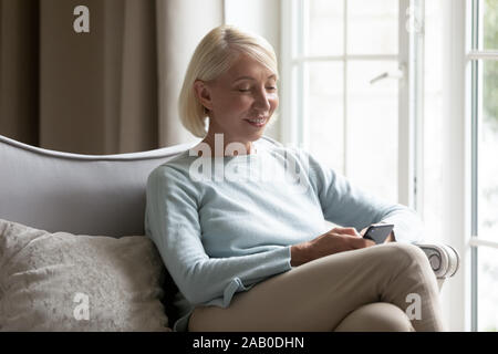 60s donna bionda utilizzando smart phone per chattare online con gli amici Foto Stock