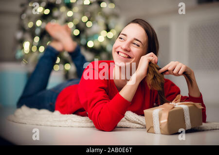 Basso angolo di seguito visualizza foto di affascinanti carino bella ragazza attraente con un regalo che indossa jeans e maglione rosso Foto Stock