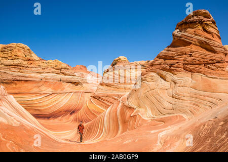 Colorate di roccia arenaria dietro un escursionista in rosso e marrone come egli cammina attraverso l'onda in Northern Arizona. Arenaria striate crea molte curve e int Foto Stock