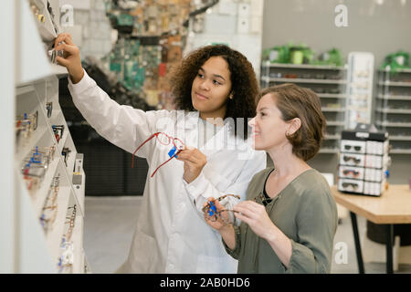 Consulente di ottica in camice bianco e il suo cliente in piedi da display con occhiali Foto Stock