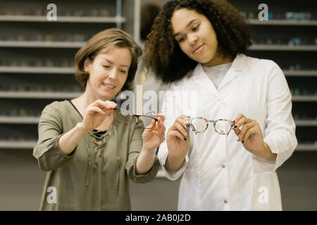 Consulente di giovani di ottica shop e client maturo confrontare occhiali Foto Stock