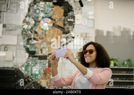 Giovane donna allegra in occhiali da sole rendendo selfie in ottica contemporanea shop Foto Stock
