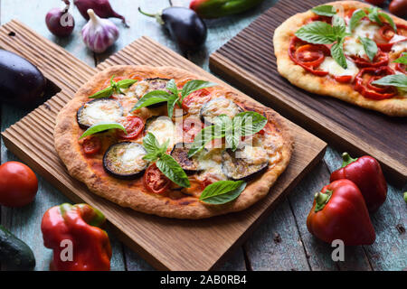 Pasto vegetariano. Le pizze fatte in casa con melanzane, peperoni, pomodori, mozzarella e basilico su pannelli di quercia servita con materie prime closeup Foto Stock