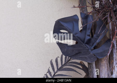 Monstera foglie nere e un decor tropicale contro una parete di luce, alla moda dettagli interni Foto Stock