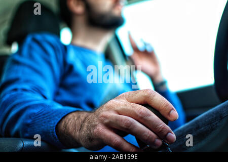 Il pendolarismo per lavoro. Man mano che tiene una marcia durante la guida. Stretti concentrati. tenere in mano la leva di cambio marcia o il livello. Vista ravvicinata all'interno dell'auto. Foto Stock