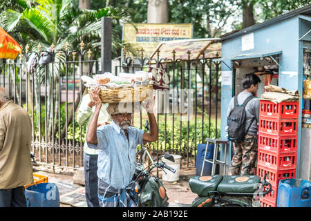 Bangalore, India, strade di Bengaluru città indiana indù vecchio uomo che porta il cestello con arachidi in vendita sulla testa, vestito di lungi Foto Stock
