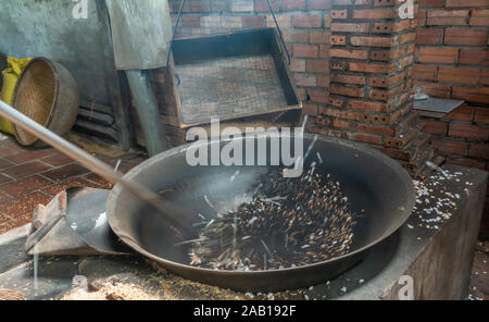 In Cai Be, Mekong Deltal, Vietnam - Marzo 13, 2019: Closeup di annerito chicchi di riso a partire da pop in nero iva riscaldato con fuoco sotto contro marrone b Foto Stock