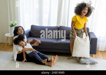 La mamma e i bambini nel soggiorno i bambini giocando insieme di disegno sul pavimento mentre il giovane mamma un momento di relax a casa sul divano, bambina divertendosi Foto Stock