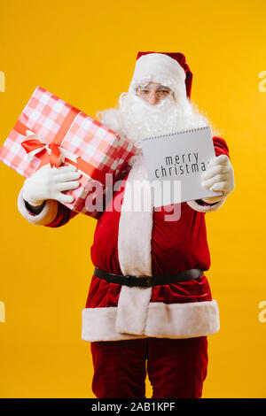 Babbo Natale con un presente in mano mostra nota con parole Buon Natale. Foto Stock