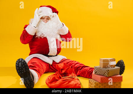 Babbo Natale seduto sul pavimento con le sue gambe divaricate, stanchi di imballaggio presenta Foto Stock