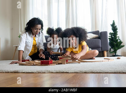 La mamma e i bambini nel soggiorno i bambini giocando insieme di disegno sul pavimento mentre il giovane mamma un momento di relax a casa sul divano, Little Boy girl divertendosi, amico Foto Stock