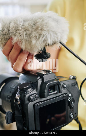 Close-up immagine di blogger di mettere il microfono sulla parte superiore della telecamera digitale professionale Foto Stock