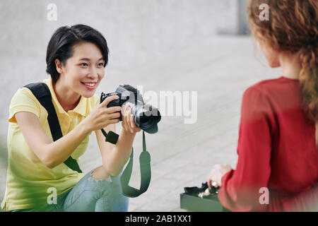 Piuttosto sorridente giovane donna godendo di scattare le foto sul modello piuttosto all'aperto Foto Stock