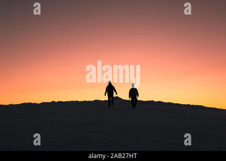 Due sagome di uomini dopo aver scalato una montagna di scendere dalla montagna al tramonto Foto Stock
