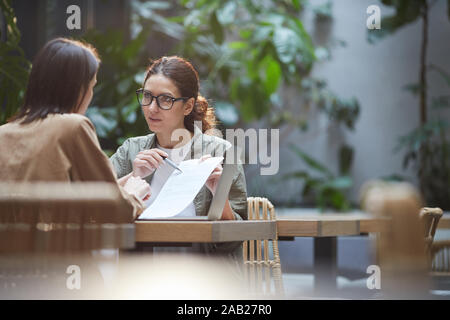 Ritratto della moderna imprenditrice puntando al contratto durante la riunione in outdoor cafe terrazza, spazio di copia Foto Stock