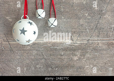 Primo piano di tre bianchi appesi Jingle Bells sul marrone scuro, rustico in legno stagionato con copia spazio. Vista dall'alto. Foto Stock