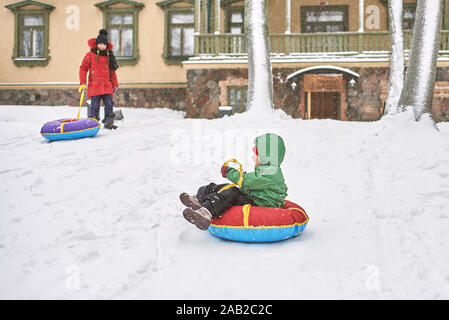 Little Boy slittino in inverno. bambino scorre giù per la montagna su una tubazione Foto Stock