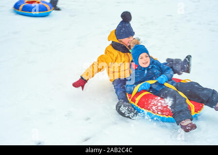 Little Boy slittino in inverno. bambino scorre giù per la montagna su una tubazione Foto Stock