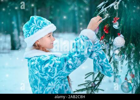 Bambina decora un albero di natale nella foresta Foto Stock