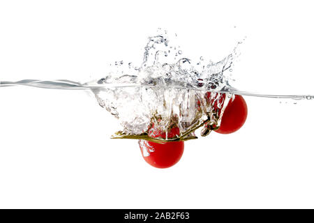 Primo piano di pomodori freschi e salutari che cadono in acqua limpida con un grande spruzzo Foto Stock