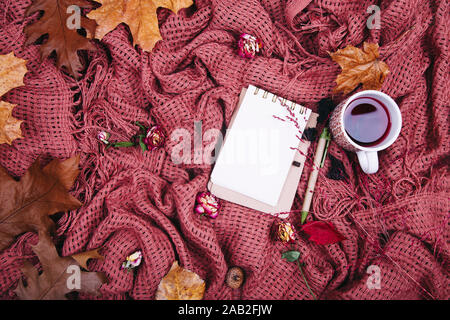 Composizione d'autunno. Tazza di tae, coperta, notebook con penna, rosa appassita. Appartamento laico, vista dall'alto, spazio di copia Foto Stock