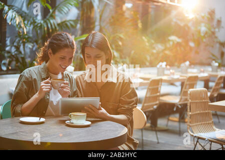 Ritratto di due donne contemporanee guardando lo schermo tablet mentre godendo incontro nella soleggiata terrazza di cura, spazio di copia Foto Stock