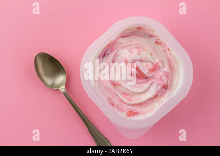 Rosa Strawberrry yogurt reale con confettura di fragole in plastica bianca tazza con cucchiaino isolati su rosa luminoso dello sfondo con spazio per il testo Foto Stock