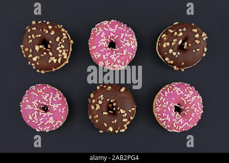 Sei ciambelle con rosa chiaro e marrone e vetri di cioccolato e zucchero spruzza su sfondo nero Foto Stock
