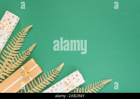 Festive sfondo verde con decorazioni in oro , sfondo con glitter shiny golden foglie di felce e confezioni regalo , piatti di laici che, vista dall'alto, spazio di copia Foto Stock