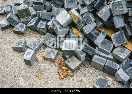 Pila di nera pietra naturale cubi per rendere pavimento esterno di piastrelle. Cataste caotiche di rotture di piastrelle su strada. Costruzione sullo sfondo di un pasticcio bac geometrica Foto Stock