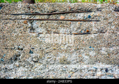 Texture di sbriciolamento parete in calcestruzzo con barre orizzontali di ferro arrugginito indotto. Attraverso danni nel vecchio ruvida la superficie in calcestruzzo con piccole pietre, dettaglio Foto Stock