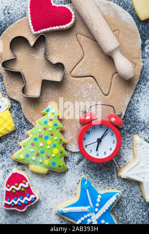 Piatto di laici tempo per biscotti di Natale il concetto di preparazione fatta di taglierine, pasta, mattarello, biscotti con glassa colorata e sveglia sul tavolo. Foto Stock