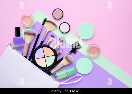 Un bianco borsa cosmetici con prodotti da trucco riversandosi su un colore di sfondo. Vista superiore Foto Stock