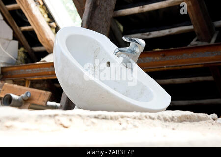 Ein Waschbecken mit Wasserhahn auf dem Fußboden in einem Abrisshaus |un lavandino con rubinetto sul pavimento in una casa di demolizione| Foto Stock