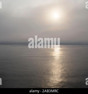 Mattina di sole risplende attraverso la nebbia sul Mare del Nord. Il mare è calmo e il sole riflette golden sulla sua superficie. Foto Stock