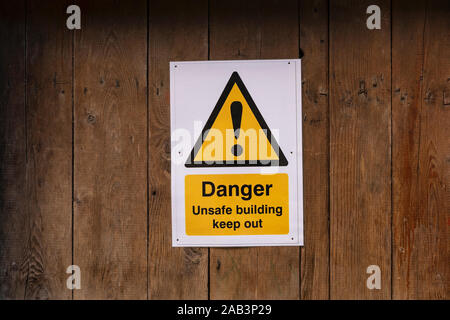 Un triangolo giallo segno con un punto esclamativo dicendo Danger Unsafe edificio tenere fuori attaccato inchiodati in un marrone porta in legno con granella horizo texture Foto Stock