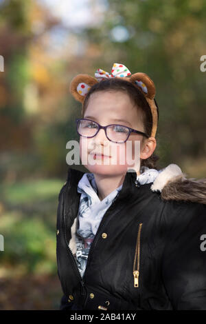 Una giovane ragazza con gli occhiali in piedi nella luce solare pezzata su un parco boschivo trail Foto Stock