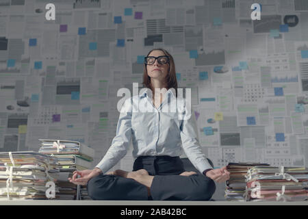 Corporate imprenditrice seduta nella posizione del loto sulla scrivania in ufficio e la pratica di meditazione, di business e di mindfulness concept Foto Stock