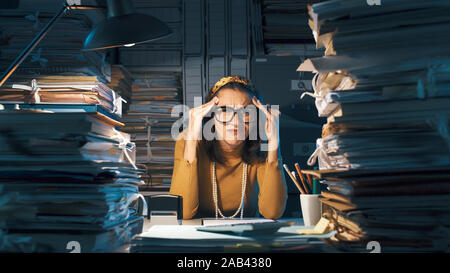 Confuso perplesso ufficio femmina lavoratore seduto alla scrivania e pensare, essa viene a contatto con i suoi templi e accigliata Foto Stock