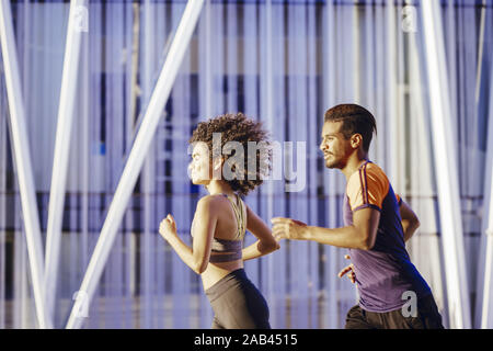Ritratto di una bella donna latina e una sportiva uomo nero correndo insieme al tramonto nella strada di città con edifici in background. urban sport Foto Stock