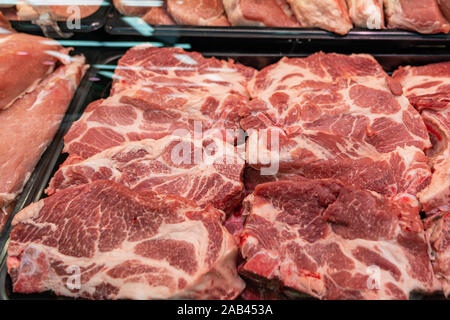 Selezione di carni di qualità presso un negozio di macellaio, macellato il maiale in un espositore refrigerato sotto vetro, vicino. Foto Stock