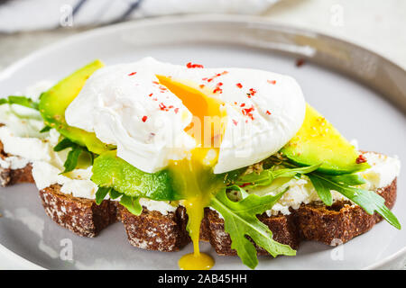 Uovo affogato toast con avocado, crema di formaggio e pane di segale su una lastra grigia. Cibo sano concetto. Foto Stock