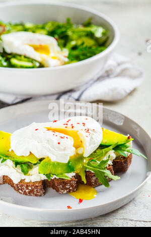 Uovo affogato toast con avocado, crema di formaggio e pane di segale su una lastra grigia. Cibo sano concetto. Foto Stock