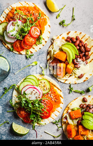 Aprire vegane tortilla avvolge con patate dolci, fave, avocado, pomodori, zucca e piantine su sfondo grigio, piatto di laici che, vista dall'alto. Vegano sano f Foto Stock