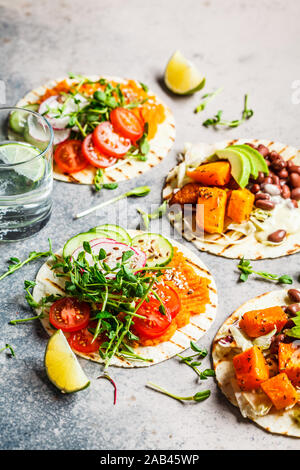 Aprire vegane tortilla avvolge con patate dolci, fave, avocado, pomodori, zucca e piantine su sfondo grigio, piatto laici. Sano cibo vegan concep Foto Stock