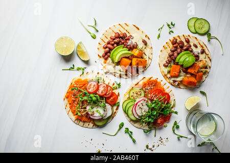 Aprire vegane tortilla avvolge con patate dolci, fave, avocado, pomodori, zucca e piantine su uno sfondo bianco, vista dall'alto, piatto laici. Vegano sano Foto Stock