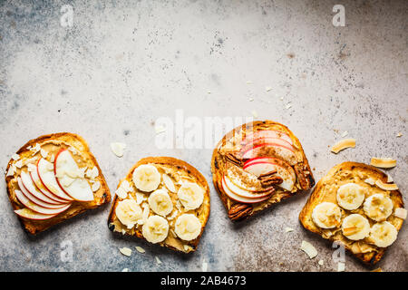 Burro di arachidi toast con banana e mela su sfondo grigio, piatto laici. Foto Stock