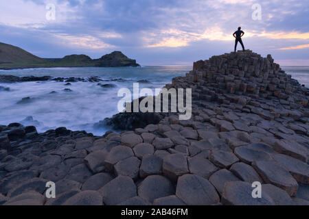 Silhouette di una persona in piedi al Giant Causeway rocce al tramonto in Irlanda del Nord Foto Stock