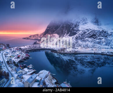 Vista aerea della montagna innevata, villaggio sulla costa del mare, cielo colorato Foto Stock