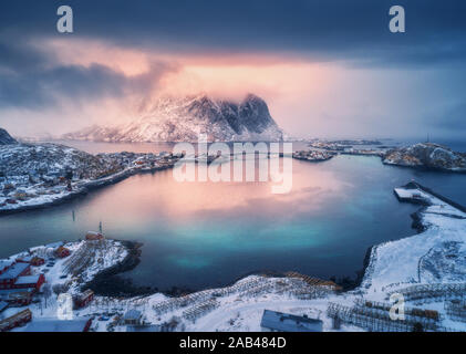 Vista aerea della montagna innevata, villaggio sulla costa del mare, cielo colorato Foto Stock